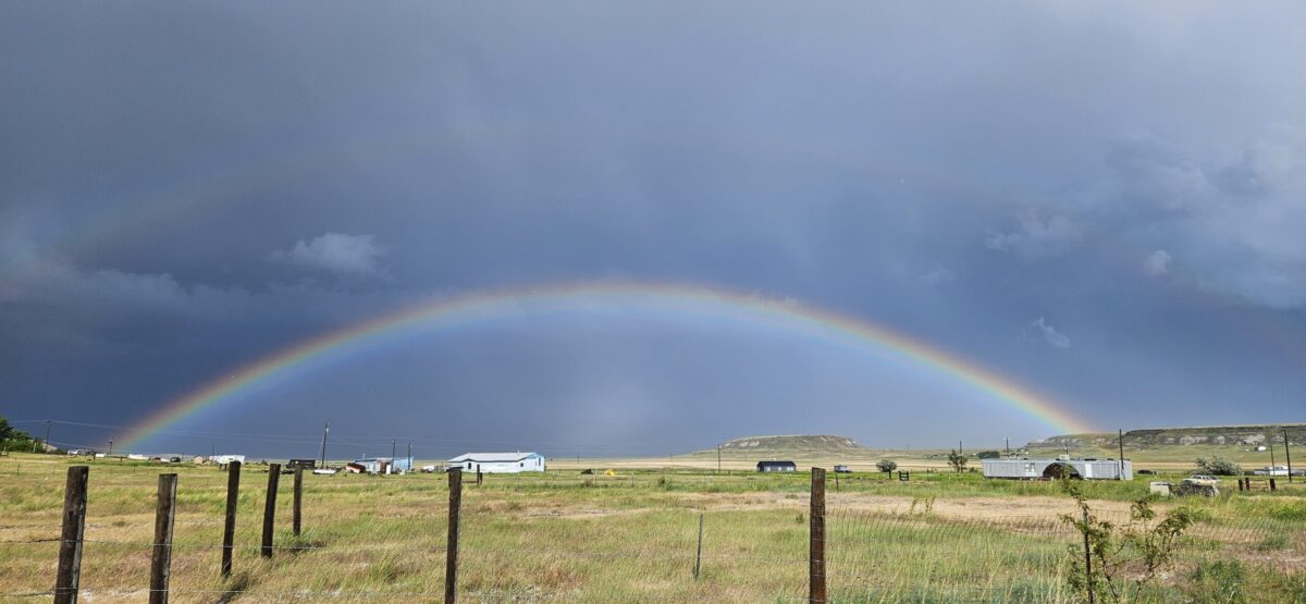 A rainbow curves over a Montana prairie landscape with a small butte in the background.
