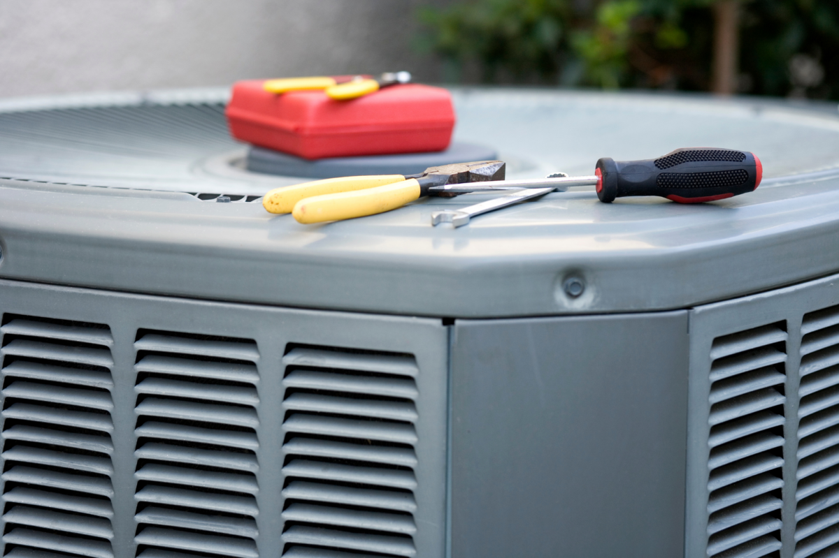 An outdoor unit with tools on top while a homeowner works through an AC troubleshooting checklist.