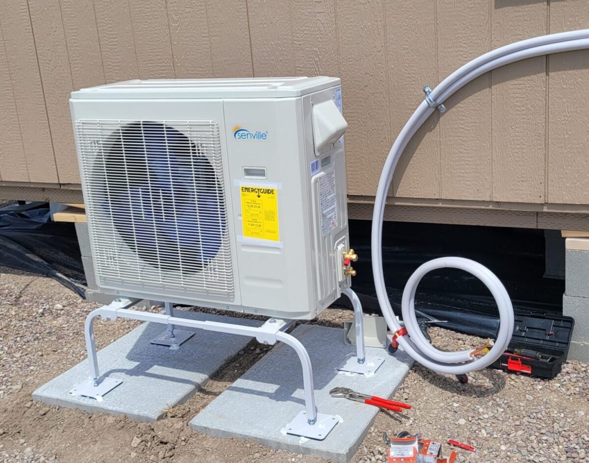 Ductless mini split outdoor unit on a stand beside a small Montana home.